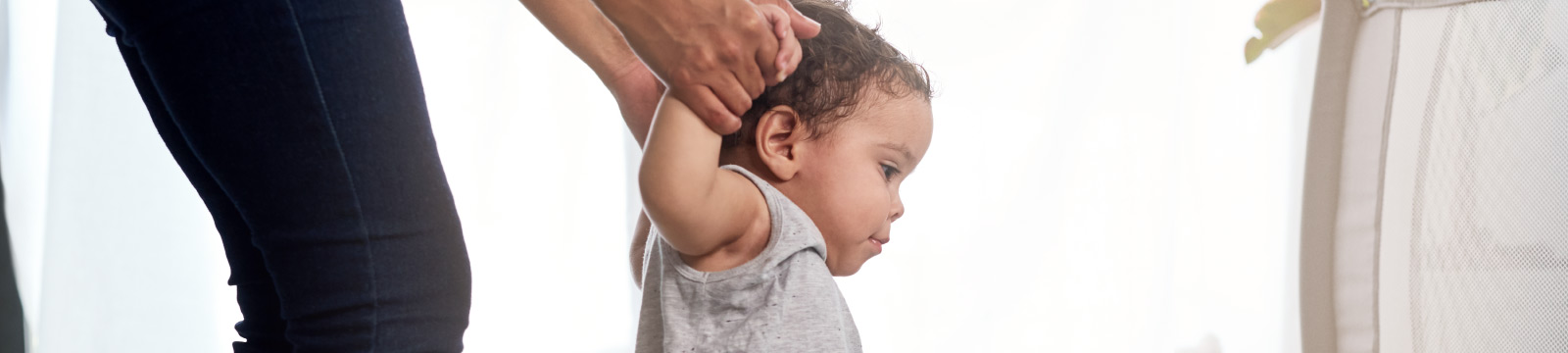 Young child takes first steps while holding on to mom's hands.